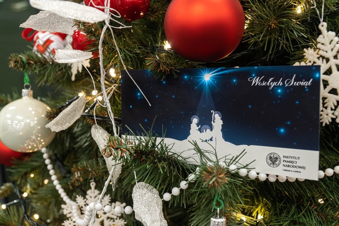 Kartka świąteczna od IPN Lublin na tle ubranej choinki