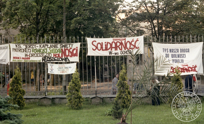 Transparenty: KS. JERZY-KAPŁANIE ŚWIĘTOŚCI PATRONUJ ROLNICZEJ SOLIDARNOŚCI W DRODZE DO WOLNOŚCI. WOLNI I SOLIDARNI ROLNICY INDYWIDUALNI WŁOSZCZOWA, SOLIDARNOŚĆ W-WA OCHOTA, TYŚ NASZĄ DROGĄ DO WOLNOŚCI I POKOJU I SOLIDARNIE Z OJCEM ŚWIĘTYM ZWYCIĘŻYMY ZŁO DOBREM-SOLIDARNOŚĆ MOKOTÓW zawieszone na ogrodzeniu kościoła pw. św. Stanisława Kostki w Warszawie. 14 VI 1987 r. Zbiór AIPN.